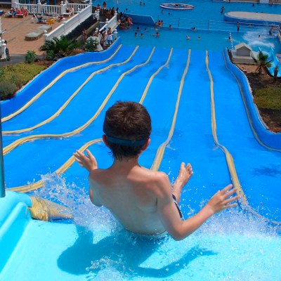 Child sliding down a blue water slide into a pool with people swimming.