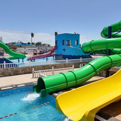 Water park with colorful slides, including green and yellow, leading into a pool under a clear blue sky.