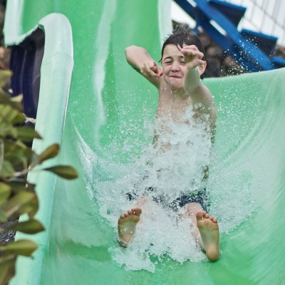 Child sliding down a green water slide with arms raised and water splashing.