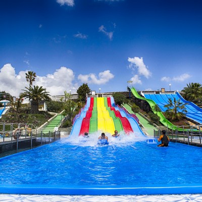 People enjoying water slides at a colorful water park under a blue sky.