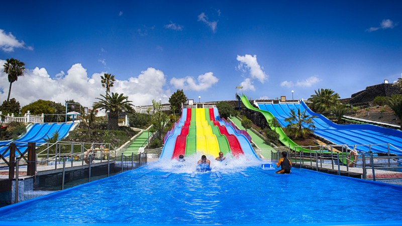 People enjoying water slides at a colorful water park under a blue sky.