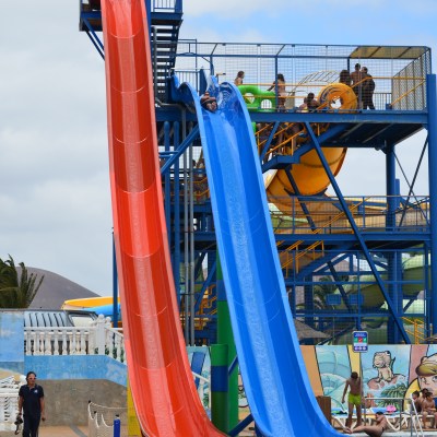Colorful water slides with people at a water park under a cloudy sky.