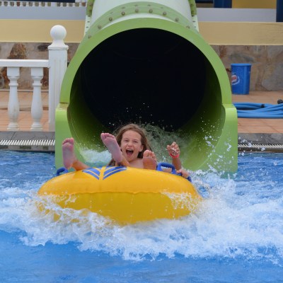Child on yellow raft coming out of water slide into pool.