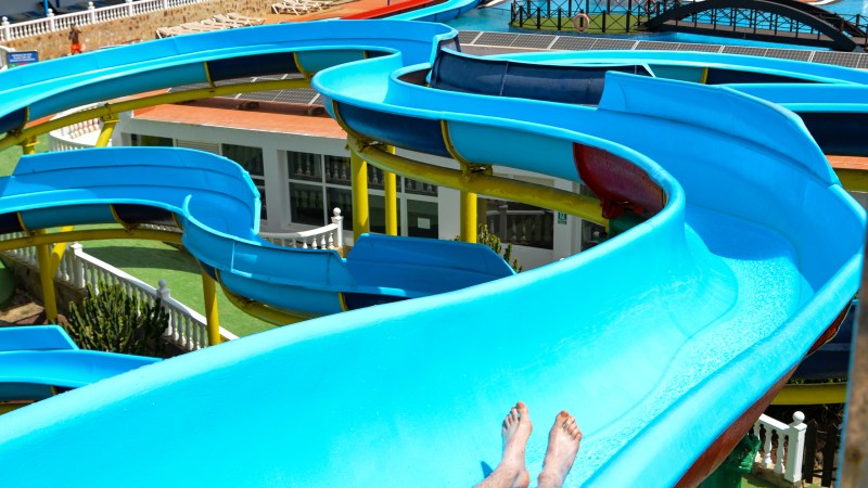 Person sliding down a blue water slide at a water park with multiple slides in the background.