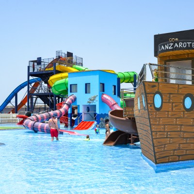 Water park with colorful slides, a pirate ship structure, and people swimming in the pool.