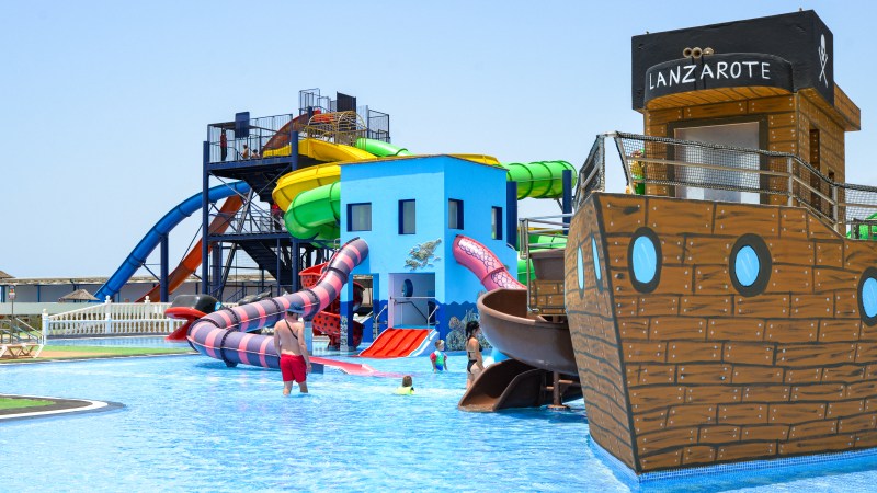 Water park with colorful slides, a pirate ship structure, and people swimming in the pool.