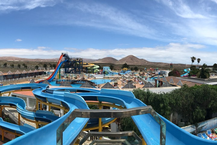Panoramic view of a water park with winding slides, pools, and distant hills under a blue sky.