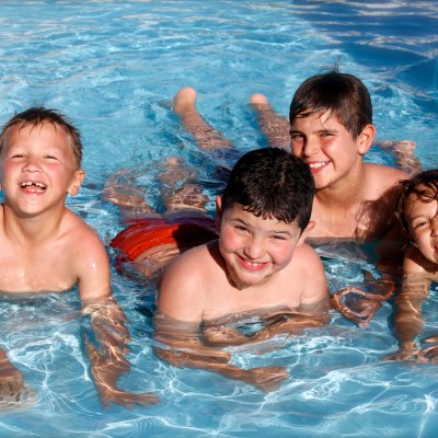 Four children smiling and playing in a swimming pool on a sunny day.