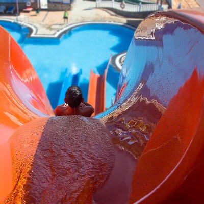Person going down a bright orange water slide towards a pool.