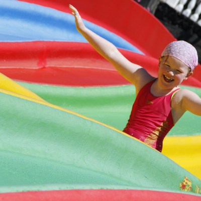 Child in red swimsuit smiling on colorful water slide with arms raised.