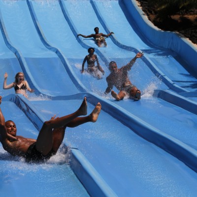 People sliding down parallel water slides at an outdoor water park.