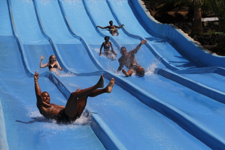People sliding down parallel water slides at an outdoor water park.