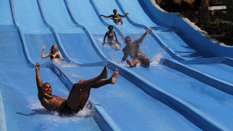 People sliding down parallel water slides at an outdoor water park.