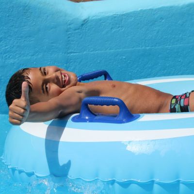 Smiling child on blue inflatable ring gives thumbs up in pool.