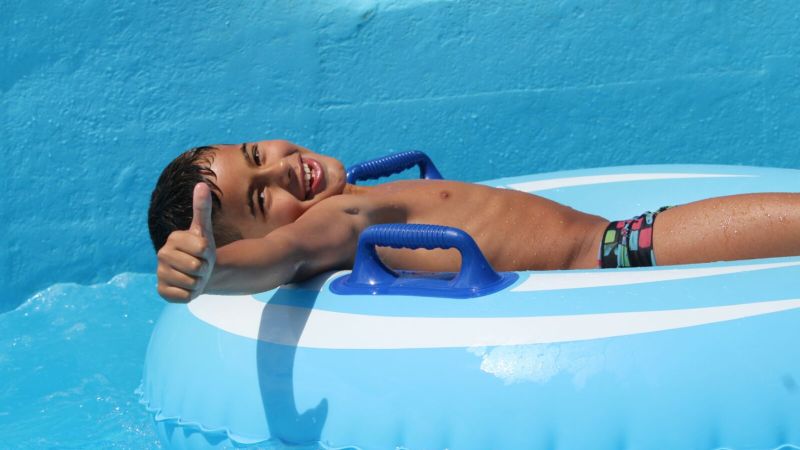Smiling child on blue inflatable ring gives thumbs up in pool.