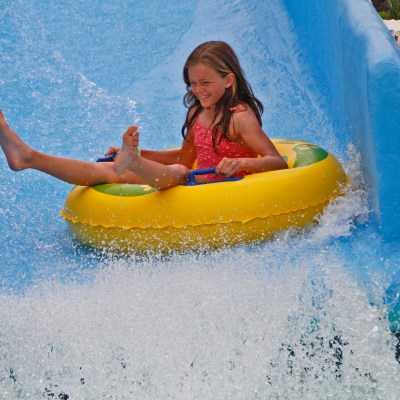 Child in an inflatable tube sliding down a watery chute at a water park.