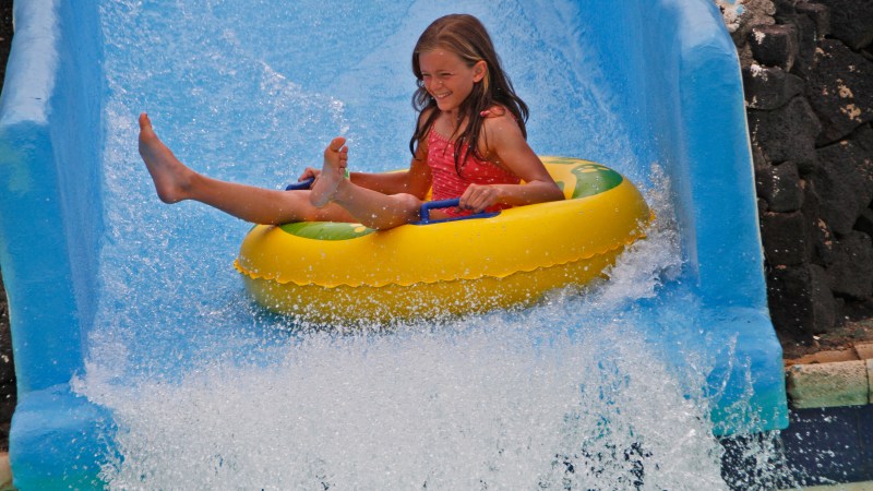 Child in an inflatable tube sliding down a watery chute at a water park.