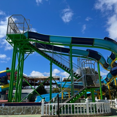 Brightly colored twisting water slide with stairs against clear blue sky.