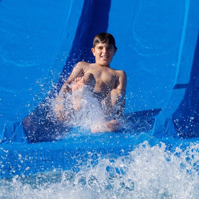 Boy sliding down a blue water slide, splashing into the pool.